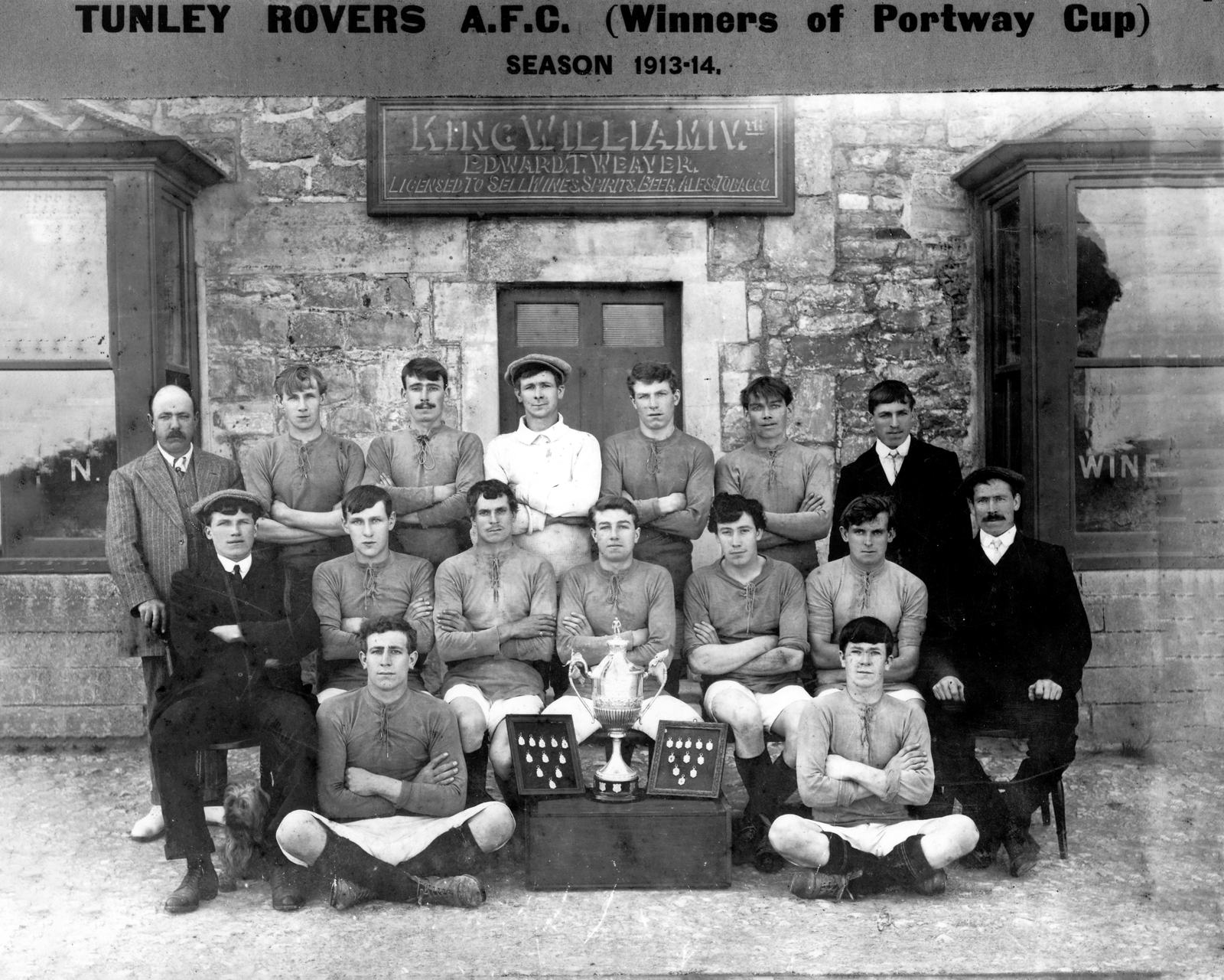 The 1913-14 Tunley Rovers team in dark shirts with the Portway Cup, posed outside the stone front of the King William IV Inn