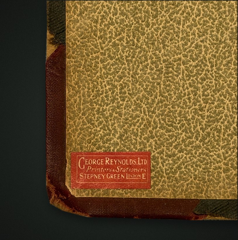 Close-up of a mottled green endpaper with a small red label reading George Reynolds Ltd, Printers and Stationers, Stepney Green, London E